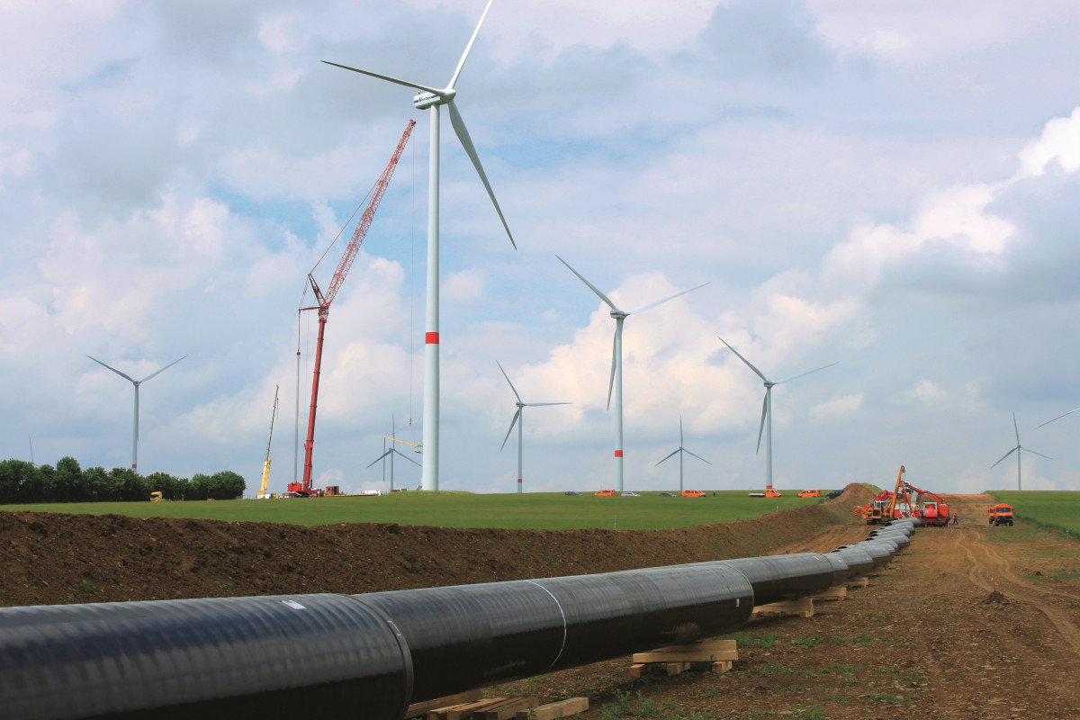 Photo shows construction of natural gas pipeline in Germany with wind power turbines in background. Photo: Open Grid Europe OGE.